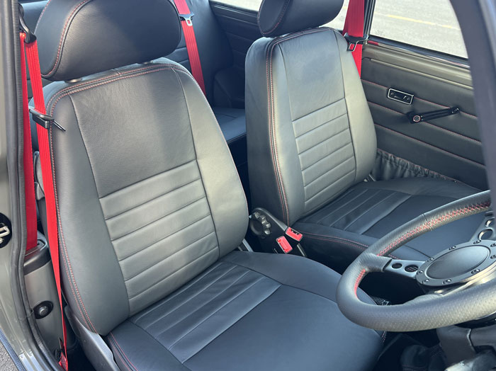 Custom-fitted black leather seats with red stitching and matching red seatbelt in a classic Mini.