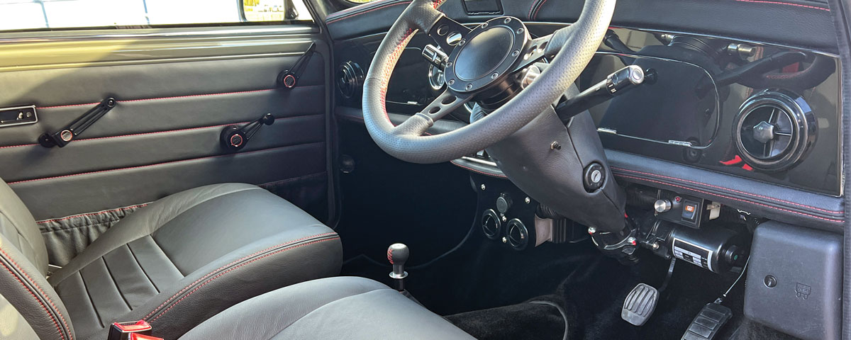 Dashboard of a bespoke Mini EV Conversion featuring a custom black leather steering wheel with red stitching.